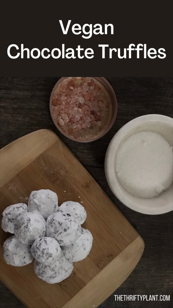 Chocolate truffles dusted with powdered sugar on a cutting board with a small bowl of pink salt and another small bowl of sugar placed next to the board.